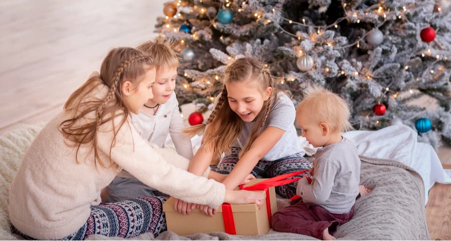 Siblings opening a gift in the family room near a Christmas tree.